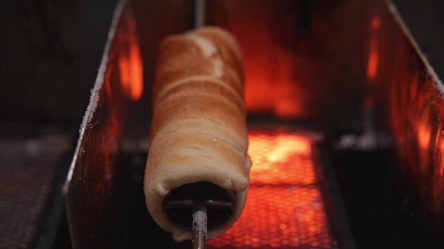 Traditional christmas chimney cake, kurtos kalacs, trdelnik, and polish kołacz slowly rotating and roasting over an open charcoal fire at a festive holiday market