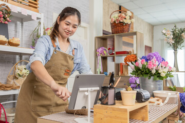 Florist shopkeeper small business owner arranging fresh flowers while checking tablet orders, creative retail startup entrepreneur, customer service focus, modern flower shop lifestyle with technology