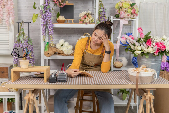 Florist shopkeeper startup small business owner feeling worried about business growth, reviewing expenses and orders at flower shop counter, facing financial concern, woman shop entrepreneur headache
