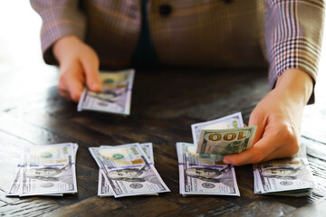 Female hands counting American one hundred dollar bills against the background of smaller bills of...