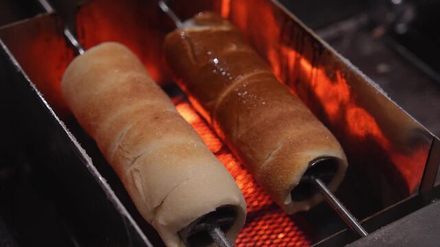 Traditional christmas chimney cake, kurtos kalacs, trdelnik, and polish kołacz slowly rotating and roasting over an open charcoal fire at a festive holiday market