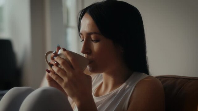 woman sipping tea or coffee in a cosy living room setting. Warm lighting.