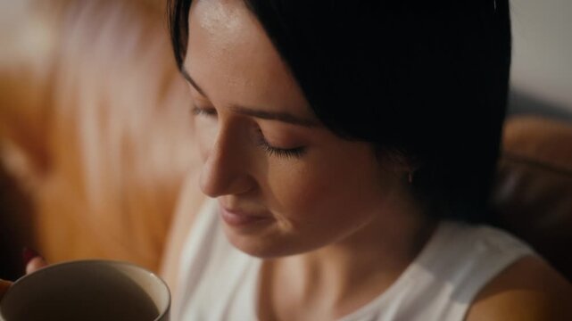 woman sipping tea or coffee in a cosy living room setting. Warm lighting.
