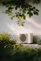 Outdoor air conditioning unit set against a white wall and some green plants.