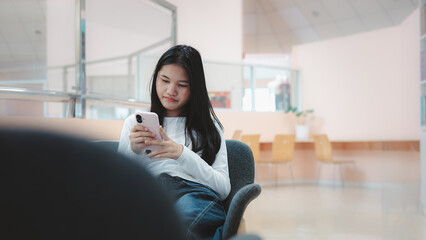 Asian woman using smartphone in modern coworking space or office lounge