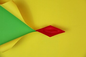 A red origami paper boat tearing yellow paper on a green background, symbolizing creativity and courage, ideal for business and motivation. Copy space for text.