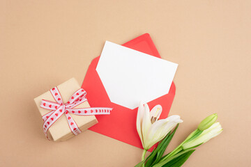 Romantic envelope with blank card, gift box and white flowers on pastel background for Valentines day message. Top view, flat lay, mockup
