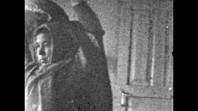 Grandmother wearing warm scarf putting on outerwear inside rural home. Everyday domestic moment in modest countryside interior, simple daily routine. Old film. Archival retro 1970s. Vintage archive