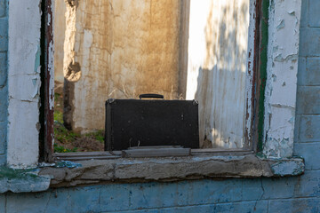 Weathered black briefcase sits on a cracked window ledge in a dilapidated building, evoking mystery and urban decay.
