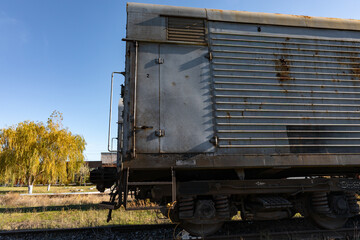 Rusty freight train car on railway in sunlight, autumn trees in background, industrial and transportation theme, horizontal composition.