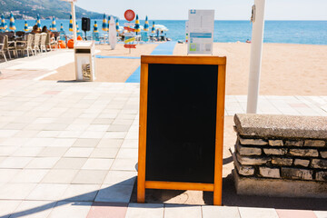 Empty blank restaurant menu board placed near beach promenade. Hospitality marketing, visual communication, and seaside dining promotion supporting tourist oriented food services. Copy space