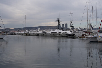 Fototapeta premium Modern marina in Athens, Greece with luxury yachts lined along the pier. Calm harbor water, sleek hulls and cloudy sky form a clean maritime travel scene.