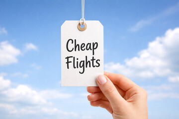 Hands holding a white paper price tag that reads cheap flights against bright blue sky