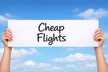 Hands holding a white paper sign that reads cheap flights against bright blue sky. Travel concept.