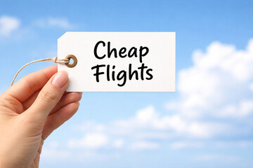 Hand holding a white paper price tag that reads cheap flights against bright blue sky
