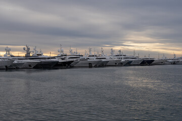 Modern marina in Athens, Greece with luxury yachts lined along the pier. Calm harbor water, sleek hulls and cloudy sky form a clean maritime travel scene.