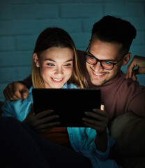 Portrait of young happy couple using tablet computer at night, using modern technology having fun...