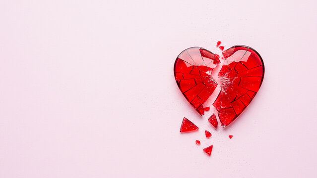 Closeup of red broken heart shape, isolated on a pink background, symbolising heartbreak, love, grief, centre aligned