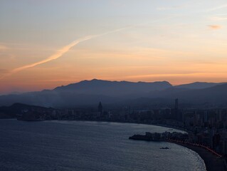 Naklejka premium dusk paints tranquil shoreline scene, serene blue hour envelops coastal city with mountains nearby