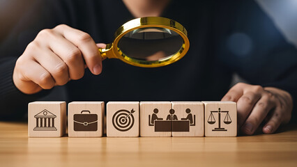 Person uses magnifying glass to examine wooden blocks featuring icons representing finance business targets meetings and legal justice systems