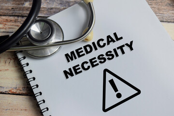 Fototapeta premium Concept of medical necessity write on book isolated on Wooden Table.