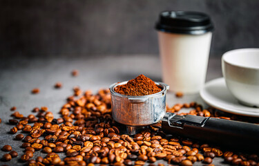 Freshly ground coffee in portafilter with roasted coffee beans and takeaway cup and coffee cup