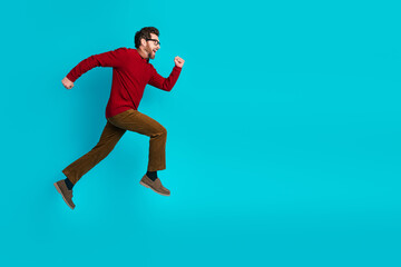 Fototapeta premium Energetic young man in red sweater and brown pants jumps in air blue background for dynamic stock photography about fitness style lifestyle and advertising appeal