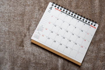 A close-up view of a spiral-bound calendar page for April 2026, displaying dates and days of the week. The calendar is set against a muted, soft background, suitable for planning and organization.