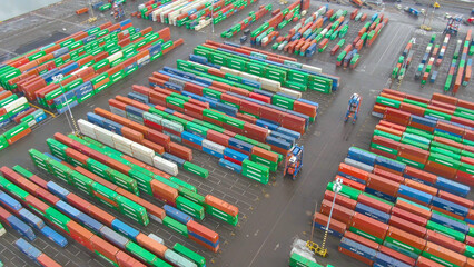 AERIAL: Industrial forklifts carry shipping containers around the colorful port.