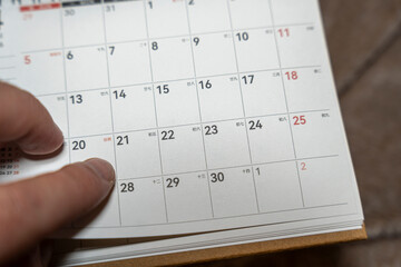 A close-up of a hand pointing at the calendar page, marking significant dates. The calendar shows various days and numbers, ideal for time management and planning topics.