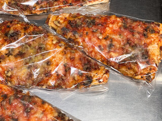 Pizza slices wrapped in plastic on a metallic surface.