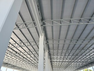 Interior view of a modern warehouse showing steel roof trusses, metal ceiling panels, and white structural columns, highlighting industrial architecture and construction details.