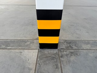 Close-up of a warehouse column painted with black and yellow safety stripes on a concrete floor, used for impact warning and industrial safety in factories and logistics facilities.