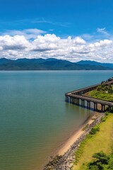 A scenic view featuring a coastal pier extending into calm waters, framed by lush greenery and mountains under a vibrant blue sky suitable for travel, nature, and relaxation-themed content,