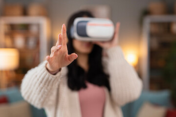 Woman wearing a virtual reality headset and interacting with digital content using hand gestures. Lifestyle technology concept focused on immersive experience and future innovation.
