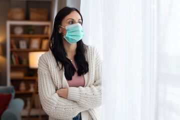 Woman wearing a protective face mask while standing at home near a window. Lifestyle healthcare concept showing safety, prevention, and health awareness.
