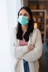 Woman wearing a protective face mask while standing indoors near a window. Vertical lifestyle healthcare image focused on safety, prevention, and health awareness.

