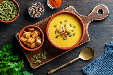 Delicious pumpkin cream soup with baked bread and pumpkin seeds in a ceramic bowl on a wooden table, closeup, top view. Healthy food concert