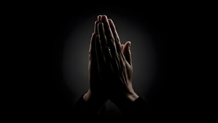 Dark still life of hands clasped in prayer silhouette, black background