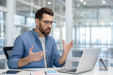 Bearded man wearing glasses communicating confidently during a virtual conference call, discussing business strategy and remote work insights from his modern office or home workspace