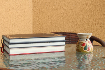 Stack of books and aromatherapy burner on top of a glass table. Horizontal shot with copy space, ideal for relaxation, reading activity, and holistic education themes.