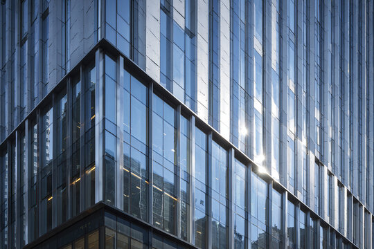 Modern glass building facade with reflective windows and metal vertical fins creating sleek contemporary architectural design in urban environment with sunlight glare