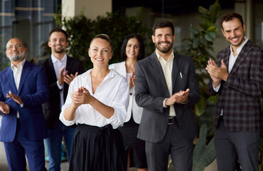 Fototapeta premium Happy applause of confident female business leader and team standing together in office. Businesswoman and excited colleagues group clapping hands to celebrate success teamwork and smiling