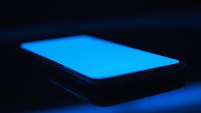A smartphone with a bright blue screen sits in the dark with blue illumination . use as multipurpose tittle intro, background. product mockup. motion graphics background