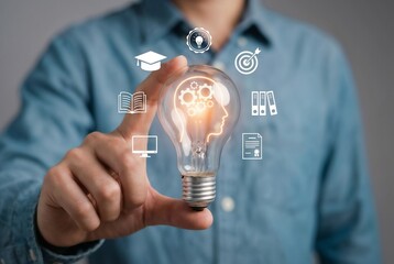 Man holding a lightbulb with a glowing silhouette of a human head and gears inside, representing brainstorming and intellect. Floating white icons representing education, graduation, books, and goals.