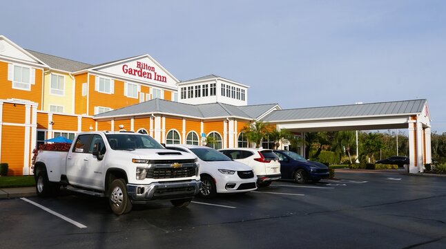 Lakeland, Florida, U.S - Jan 2, 2026 - The exterior of Hilton Garden Inn with vibrant facade, palm landscaping, and multiple vehicles parked near covered entrance.