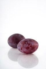 Obraz premium Ripe purple plums over white background, shallow depth of field