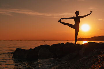 Woman practicing yoga at seaside at sunset or sunrise. Holistic Health and Mental Well-Being.