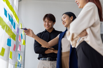 Asian businesspeople are discussing and brainstorming using colorful sticky notes on a glass board...