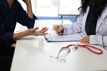 Fototapeta premium Female doctor documenting patient medical history during a consultation in a hospital office, prescribing treatment, and meticulously filling out medical records for effective care.